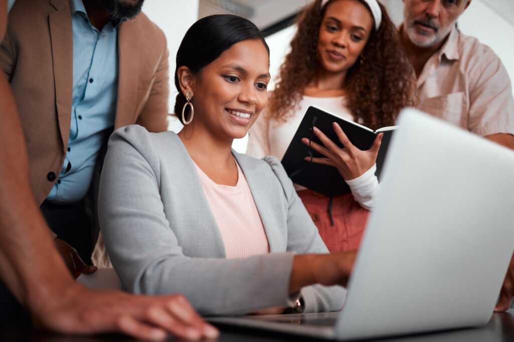 Shot of a group of businesspeople gathered around their manager using a laptop